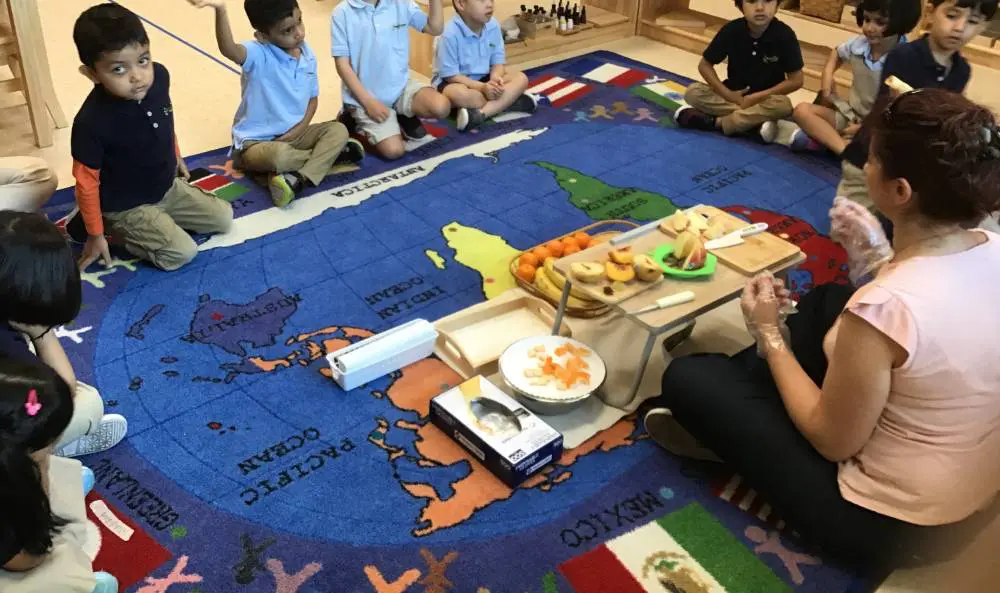 Teacher teaching student with map table cloth on fruits on it