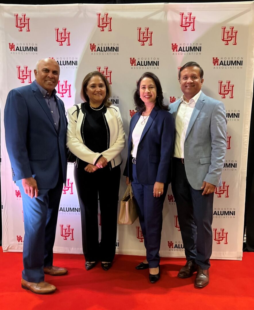 Four professionals posing at a University of Houston event with branded backdrop.