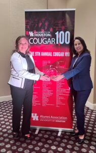 Two women shaking hands in front of a Cougar 100 banner.