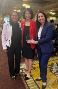 Three women in professional attire posing with an award.